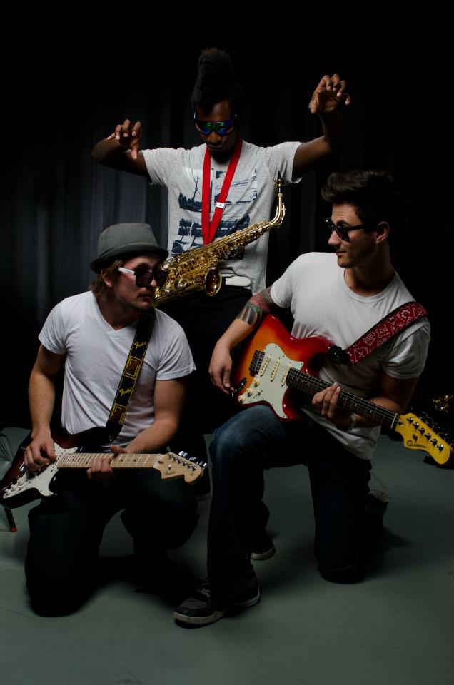 Three band members with guitars and saxophone in a studio