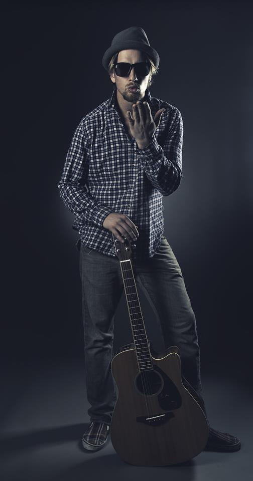 Axel in hat and sunglasses leaning on his acoustic guitar
