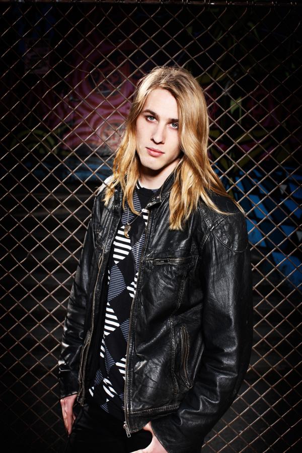 Axel in a leather jacket against a chain-link fence